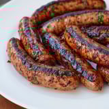 Close-up of sizzling Tunisian Merguez sausage, browned on a grill pan, showing spicy details.