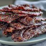 Glistening strips of Black Currant Smoky Jerky with a deep mahogany hue and cherry wood smoke swirls.