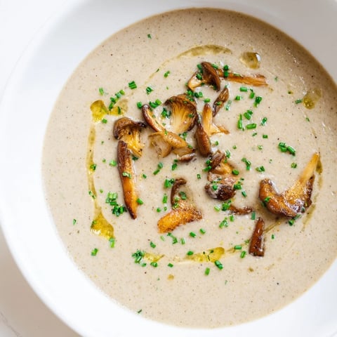 A steaming bowl of creamy mushroom bisque, garnished with fresh chives, ready to eat.