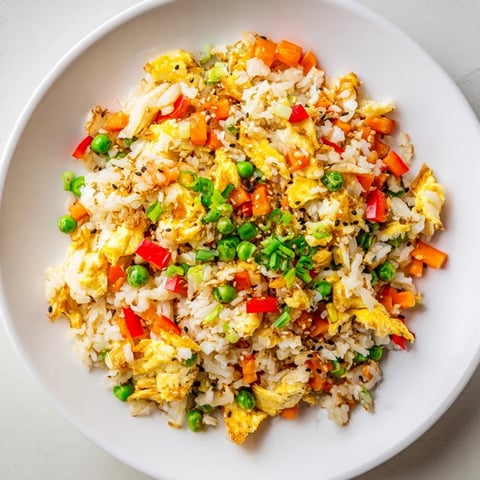 A close-up of Egg Fried Rice Classic, featuring fluffy scrambled eggs, colorful peas, carrots, and crisp scallions piled high on a white plate.