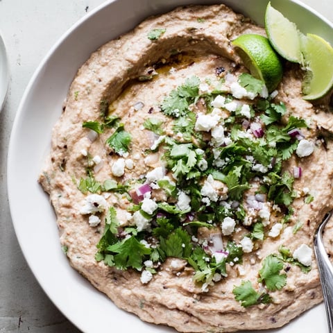 Creamy Spicy Black Bean Dip garnished with fresh cilantro, jalapeños, and lime wedges, ready for dipping with tortilla chips.  