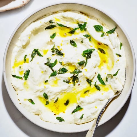 Tangy whipped feta dip, drizzled with lemon-mint, appears cool and refreshing for a flavorful appetizer.