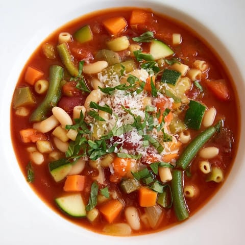 A close-up shot of the vibrant tomato basil minestrone, garnished with fresh herbs and Parmesan cheese.