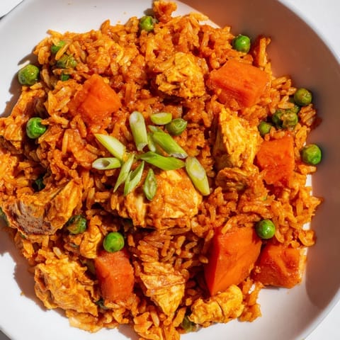 A close-up of butter chicken fried rice topped with fresh green onions, served steaming hot in a skillet.  