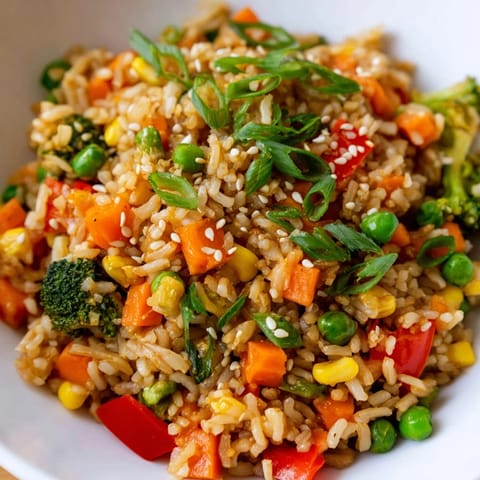 Garnished bowl of homemade Vegetable Fried Rice topped with sliced green onions and sesame seeds, served alongside a small dish of soy sauce for dipping.