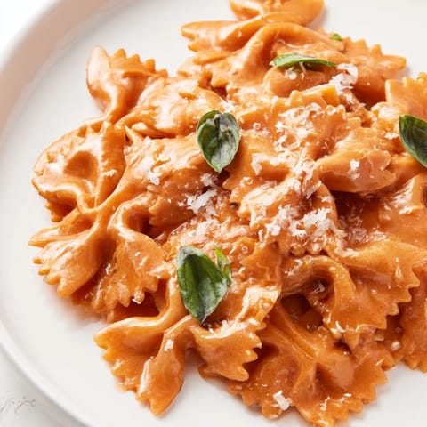 A fork lifts a twirl of Tomato Basil Bowtie Pasta, highlighting the silky, rich sauce clinging to each pasta bow.  
