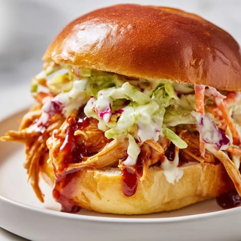 Tender pulled barbecue chicken piled high on a toasted brioche bun, topped with creamy, tangy slaw for a satisfying meal.