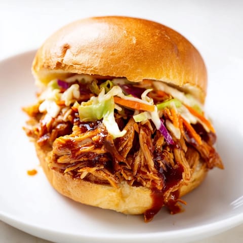 Juicy shredded chicken coated in smoky barbecue sauce spills out of a soft brioche bun, layered with crunchy, vibrant coleslaw.