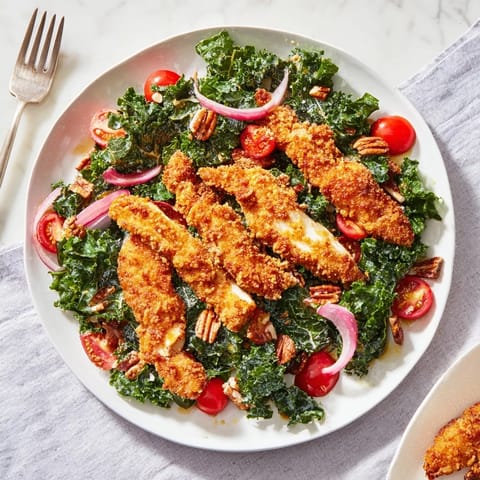 A vibrant bowl of Crispy Chicken Kale Salad topped with sliced chicken, red onion, pecans, and shaved Parmesan, ready to enjoy.  