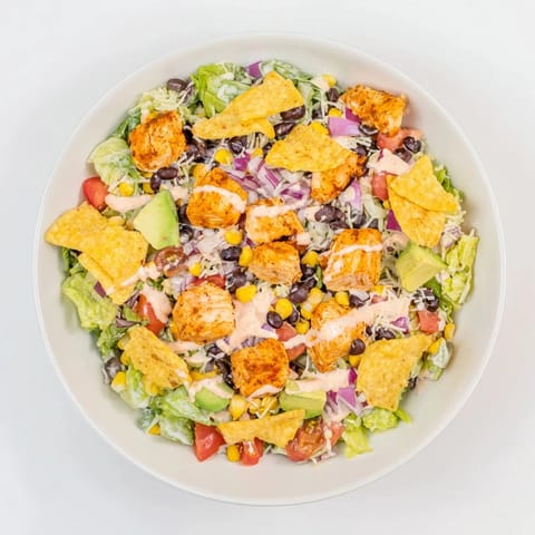 A close-up of the vibrant Chicken Taco Chopped Salad with shredded cheese, halved cherry tomatoes, red onion, and a drizzle of creamy salsa ranch dressing.