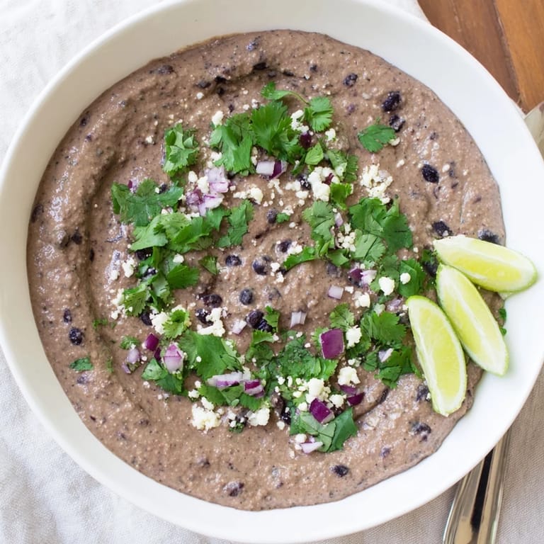 Smooth, smoky Spicy Black Bean Dip topped with cheese and fresh herbs, served with crunchy vegetable sticks for dipping.