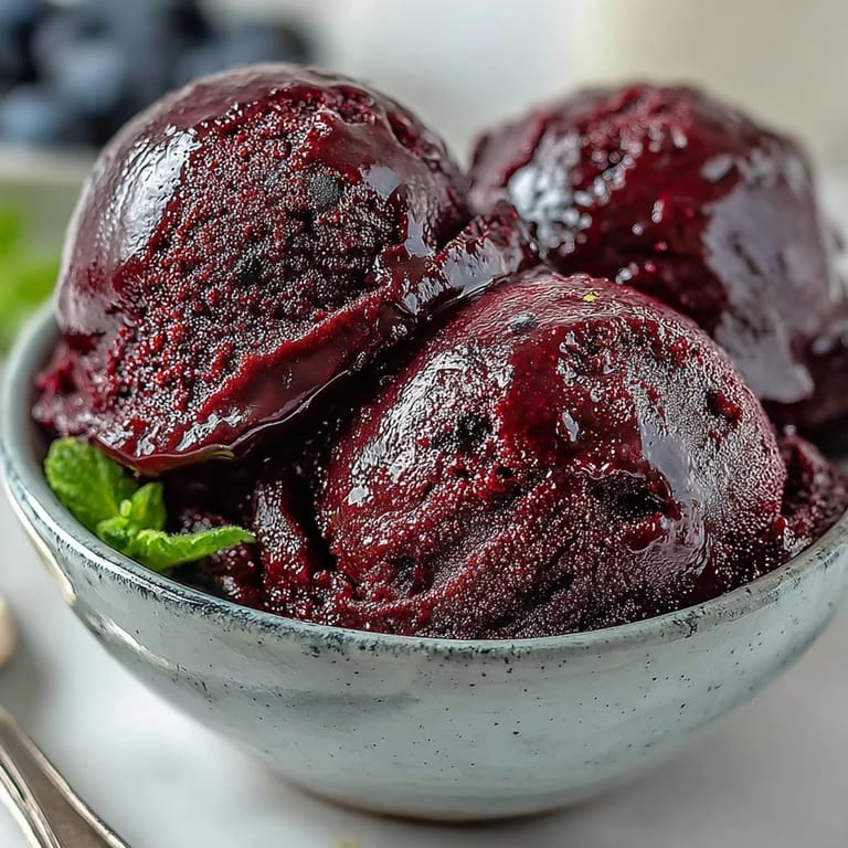 Freshly churned Black Currant Sorbet in a clear glass cup, showing off the vibrant berry color and smooth, frosty consistency.