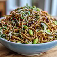 Vibrant sesame ginger noodle bowl with chilled soba noodles, crunchy cabbage, and a tangy ginger dressing topped with sesame seeds.